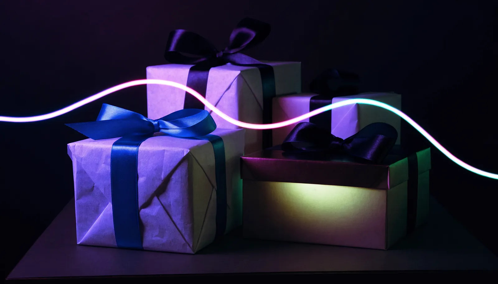 Boîtes cadeaux rubannées sur fond sombre, liseré néon
